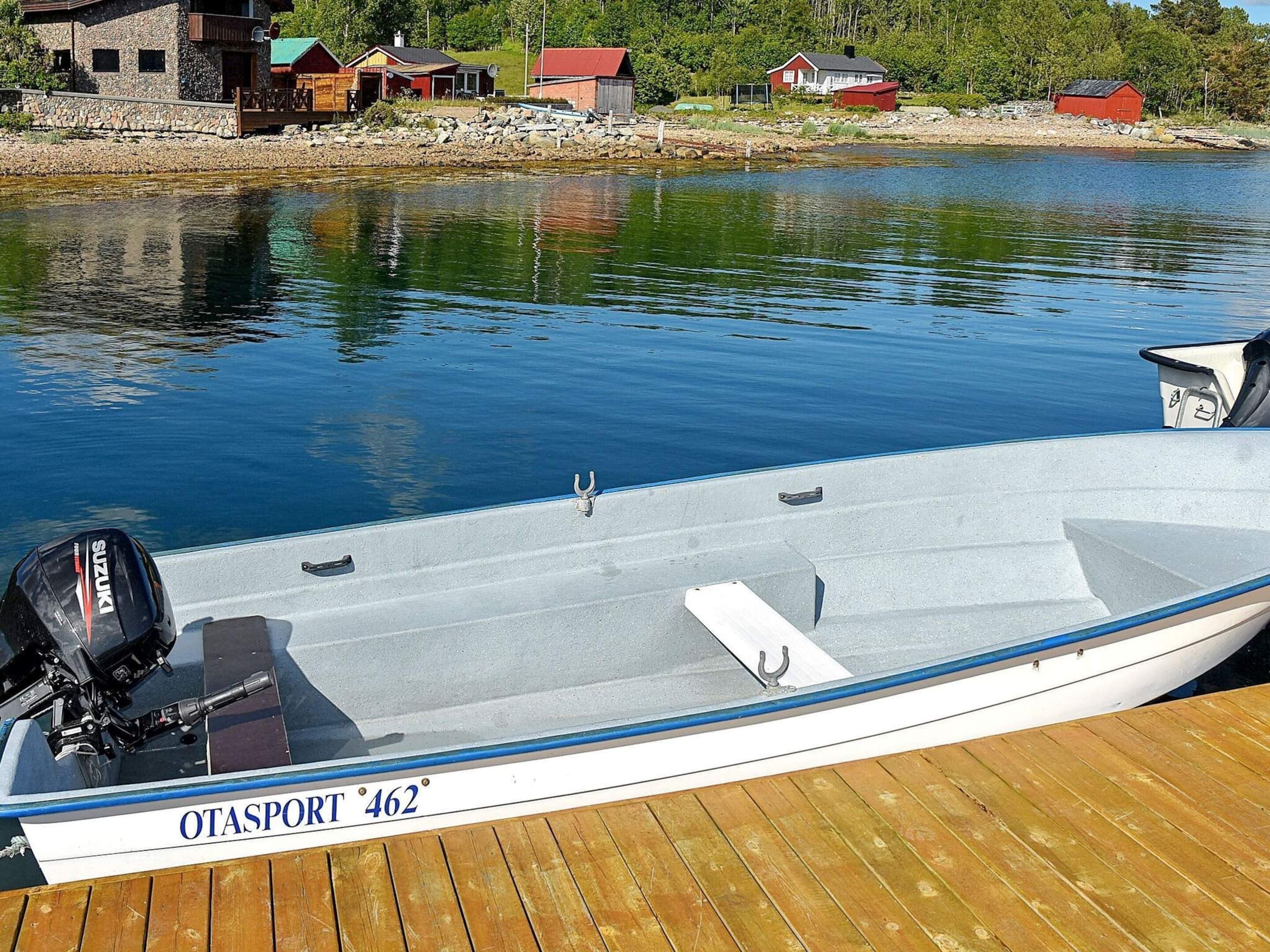 Un barco llamado 'OTASPORT 462' atracado en un muelle de madera, con un lago tranquilo y casas al fondo.