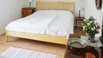 A bedroom with a wooden bed, bedside tables, a nightstand, a bedside lamp, a decorative vase with flowers, and a wooden table with a metal bowl and a wooden spoon.