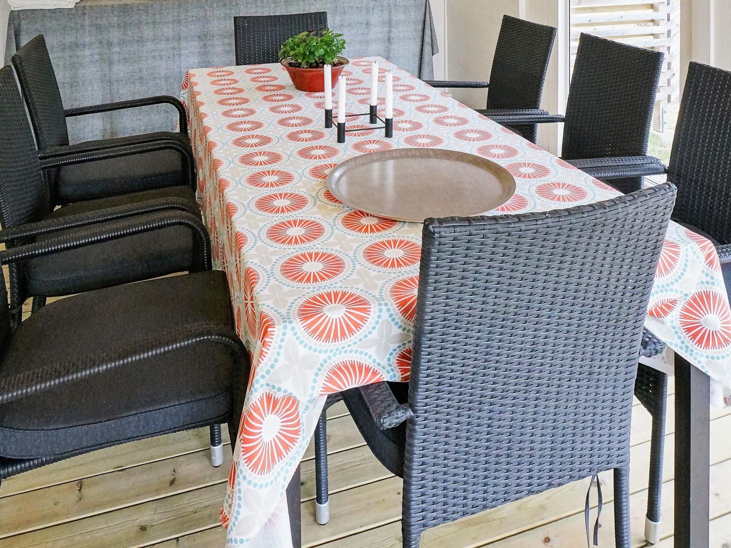 An outdoor dining area with a table covered by a patterned tablecloth, surrounded by wicker chairs.