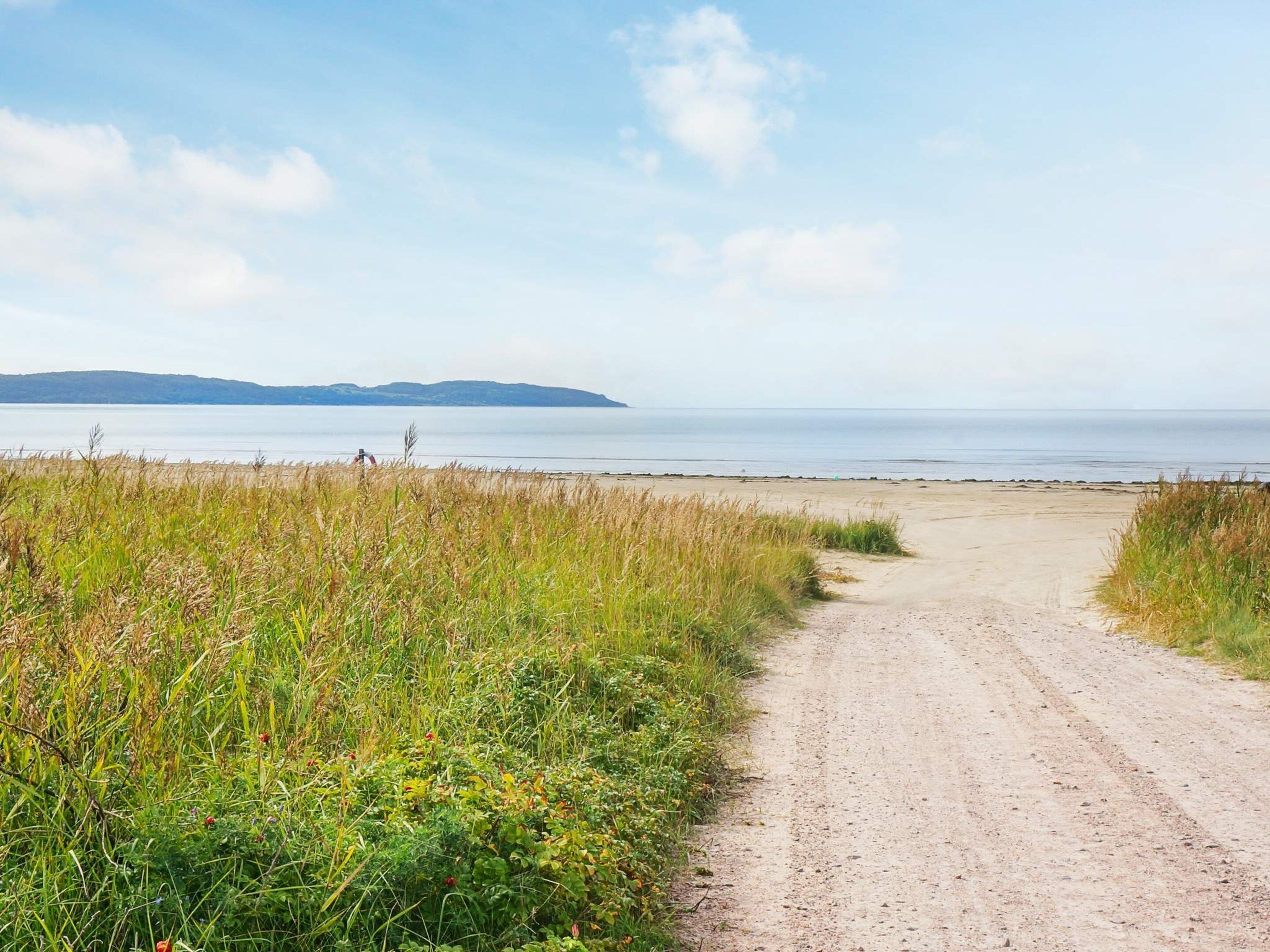 A dirt path leading to a beach with a calm sea and distant hills.