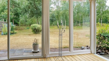 A room with large glass doors leading to a garden, a wooden deck, and a black candle holder.