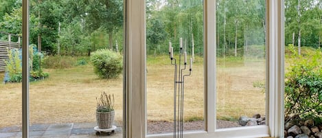 Ein Zimmer mit großen Glasüren, die zu einem Garten, einer Holzterrasse und einem schwarzen Kerzenhalter führen.