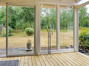 A room with large glass doors leading to a garden, a wooden deck, and a black candle holder.