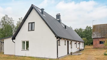 A white building with a gabled roof, a chimney, and a small porch with a bench.