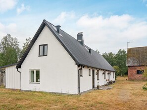 A white building with a gabled roof, a chimney, and a small porch with a bench.