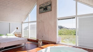 A spacious room with a large window, a bed, a wooden ceiling, and a hot tub. - 6 Person Holiday Home in Lokken-by Traum (Lokken)