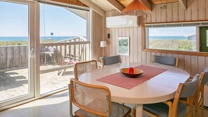 A wooden interior with a round table and chairs, large windows with ocean views, and a hanging pendant light. - 6 Person Holiday Home in Lokken-by Traum (Lokken)