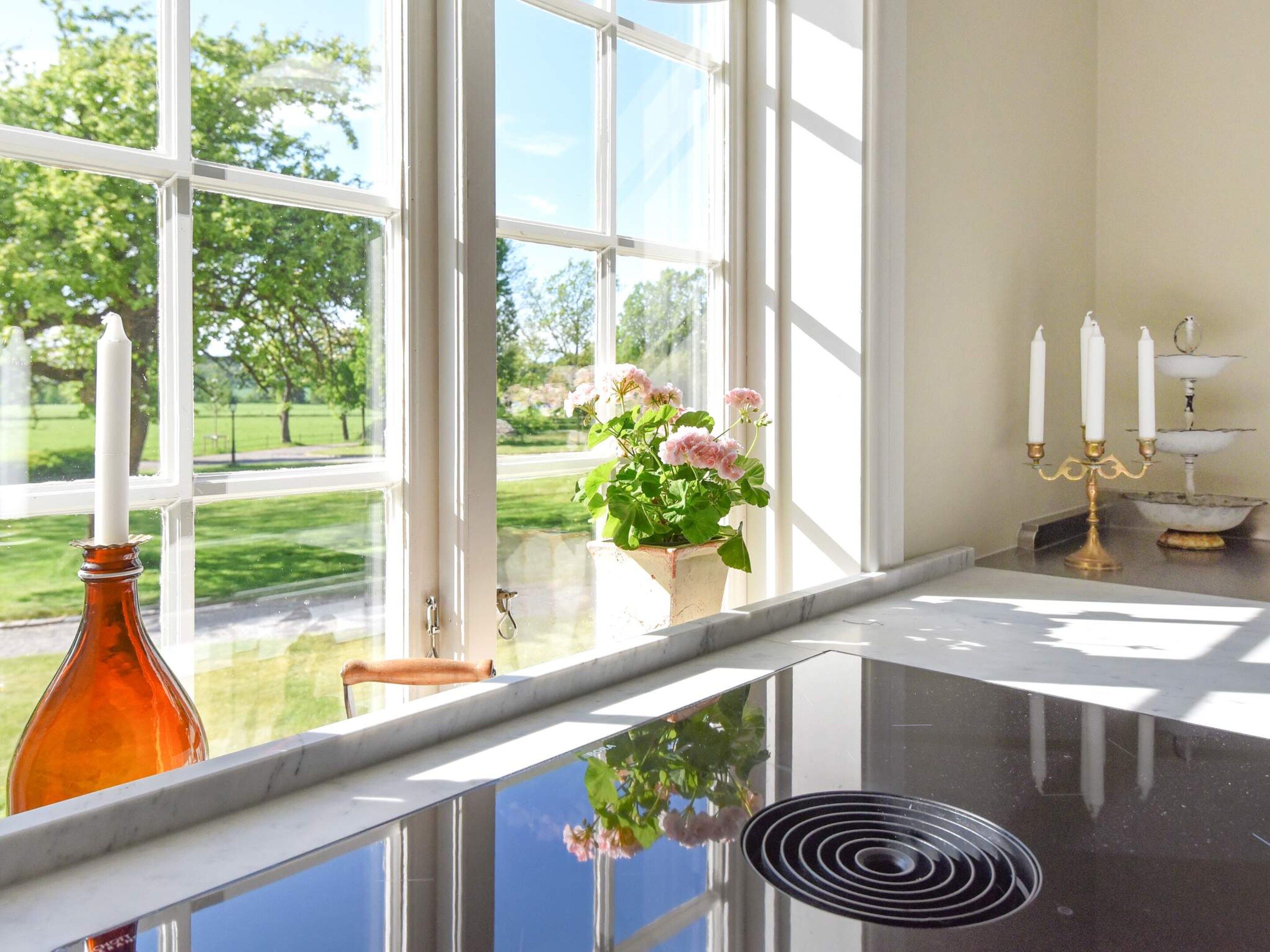 Una habitación con un ventanal grande, un florero con flores y un candelabro.