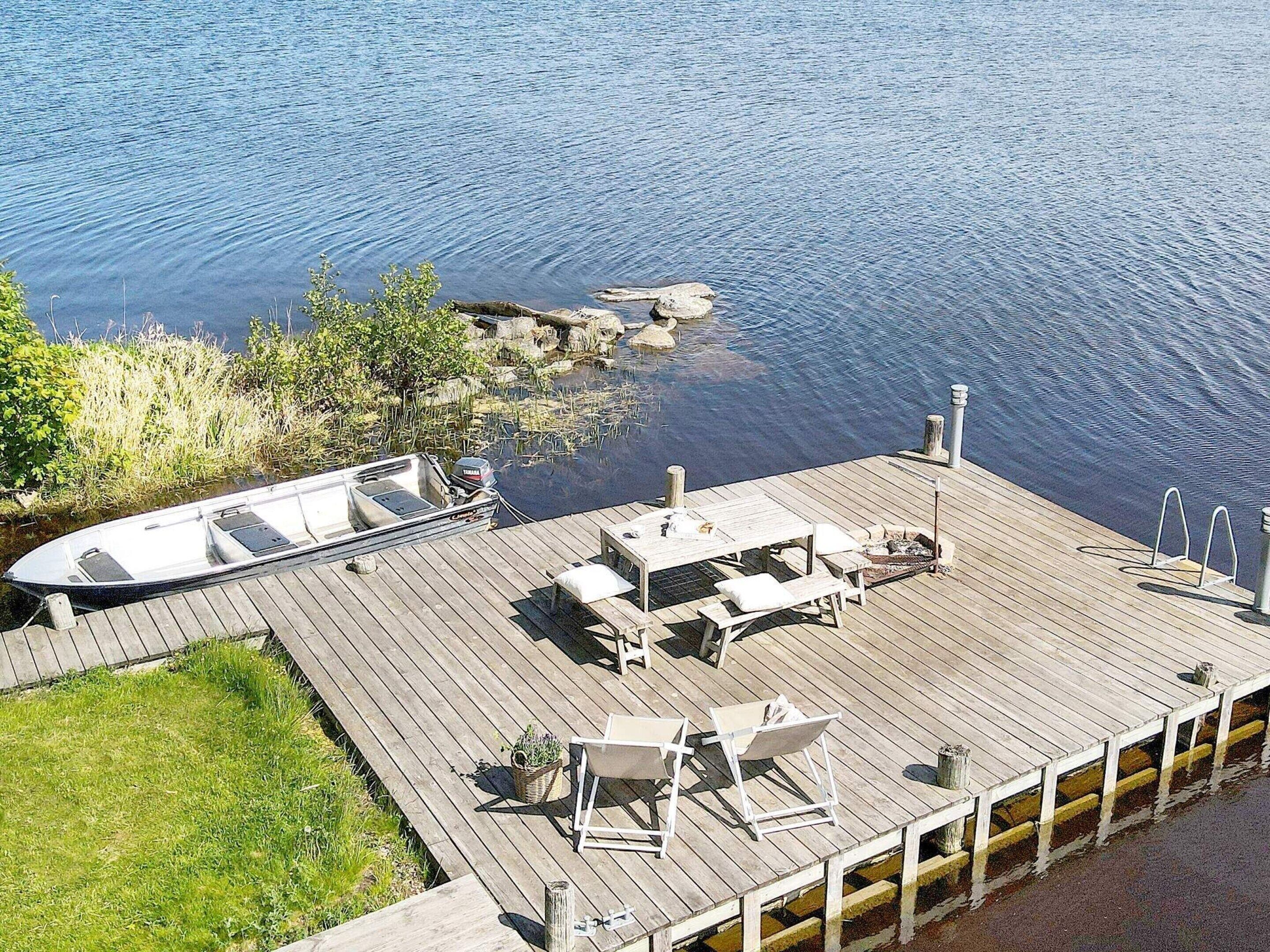 A wooden dock with a boat, outdoor seating, and a grassy area.