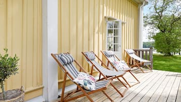A wooden deck with four striped lounge chairs and a small table, adjacent to a yellow building with a white door.