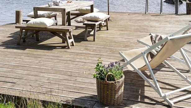 A wooden deck with a table and benches, a white lounge chair, and a wicker basket with plants. - Holiday Home in Hova (Hova)