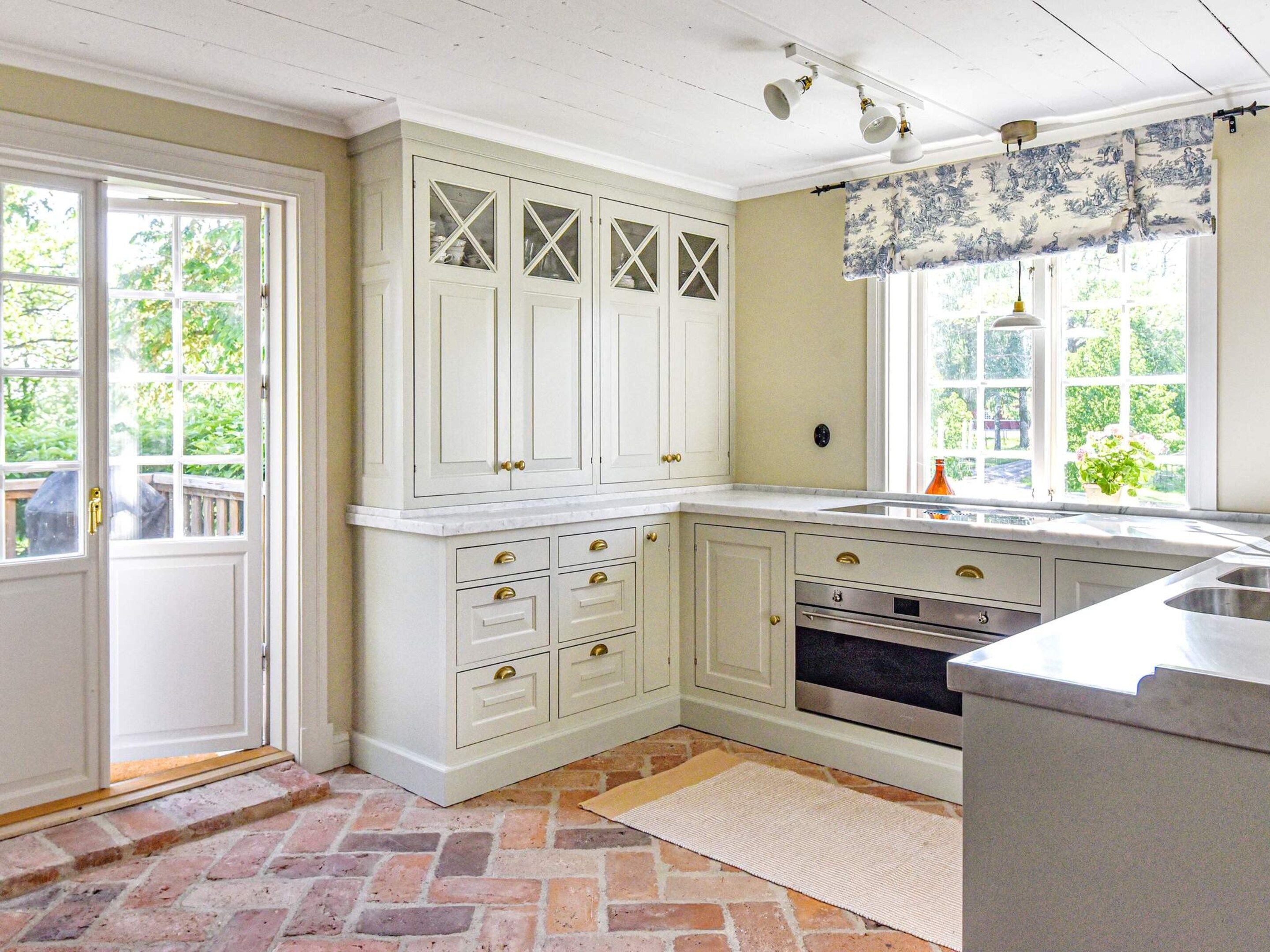 A kitchen with white cabinetry, a brick floor, and a window with a view of greenery.