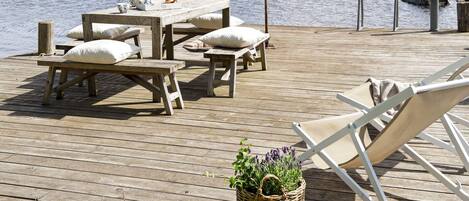 A wooden deck with a table and benches, a white lounge chair, and a wicker basket with plants.
