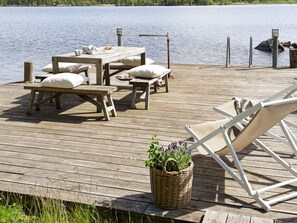 A wooden deck with a table and benches, a white lounge chair, and a wicker basket with plants. - Holiday Home in Hova (Hova)
