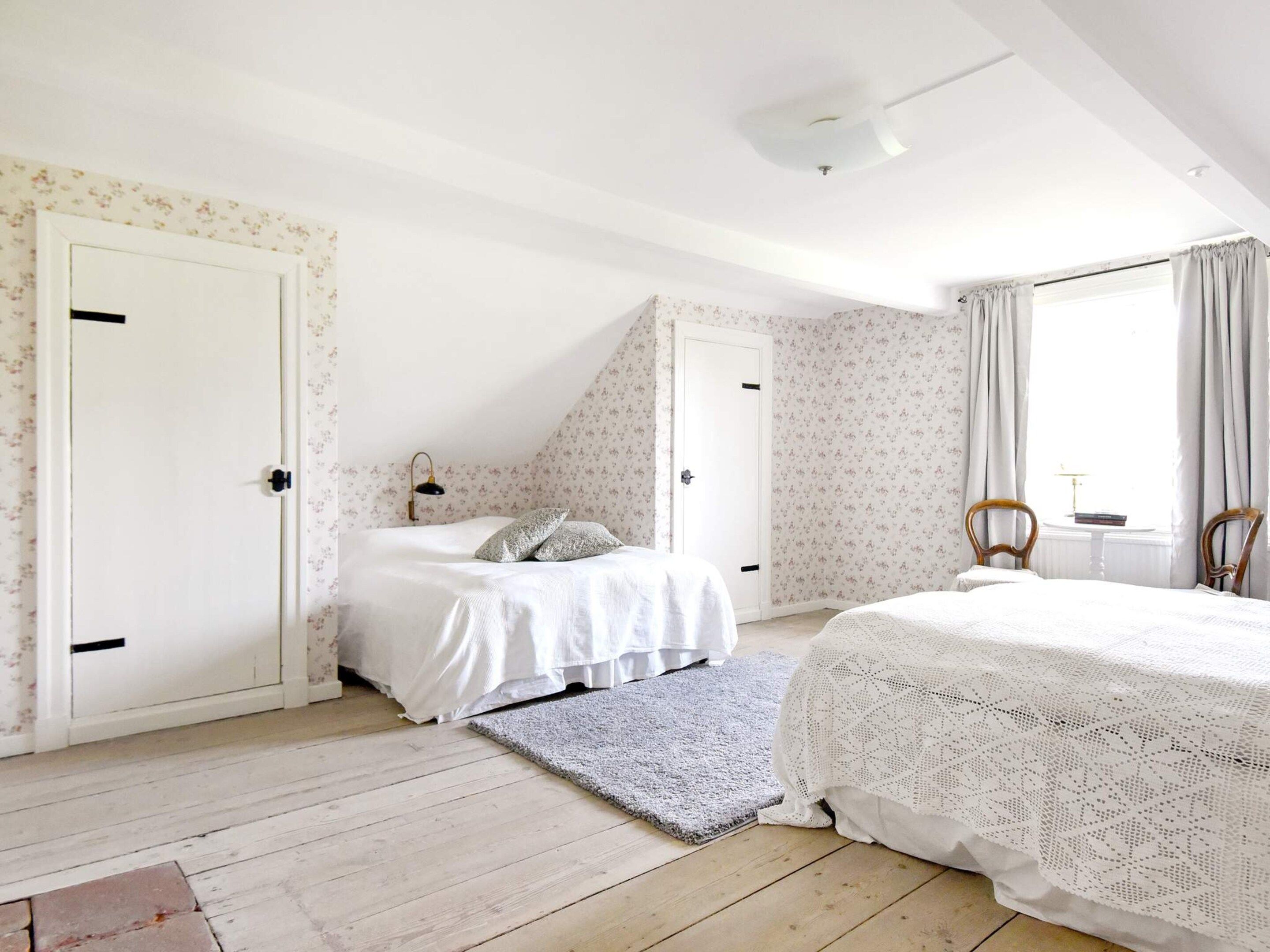 A bedroom with a bed, a chair, a small table, and a window with curtains.