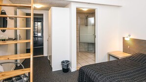 A bedroom with a loft-style bed, a wooden ladder, a small bedside table, and a view of a bathroom with a shower.