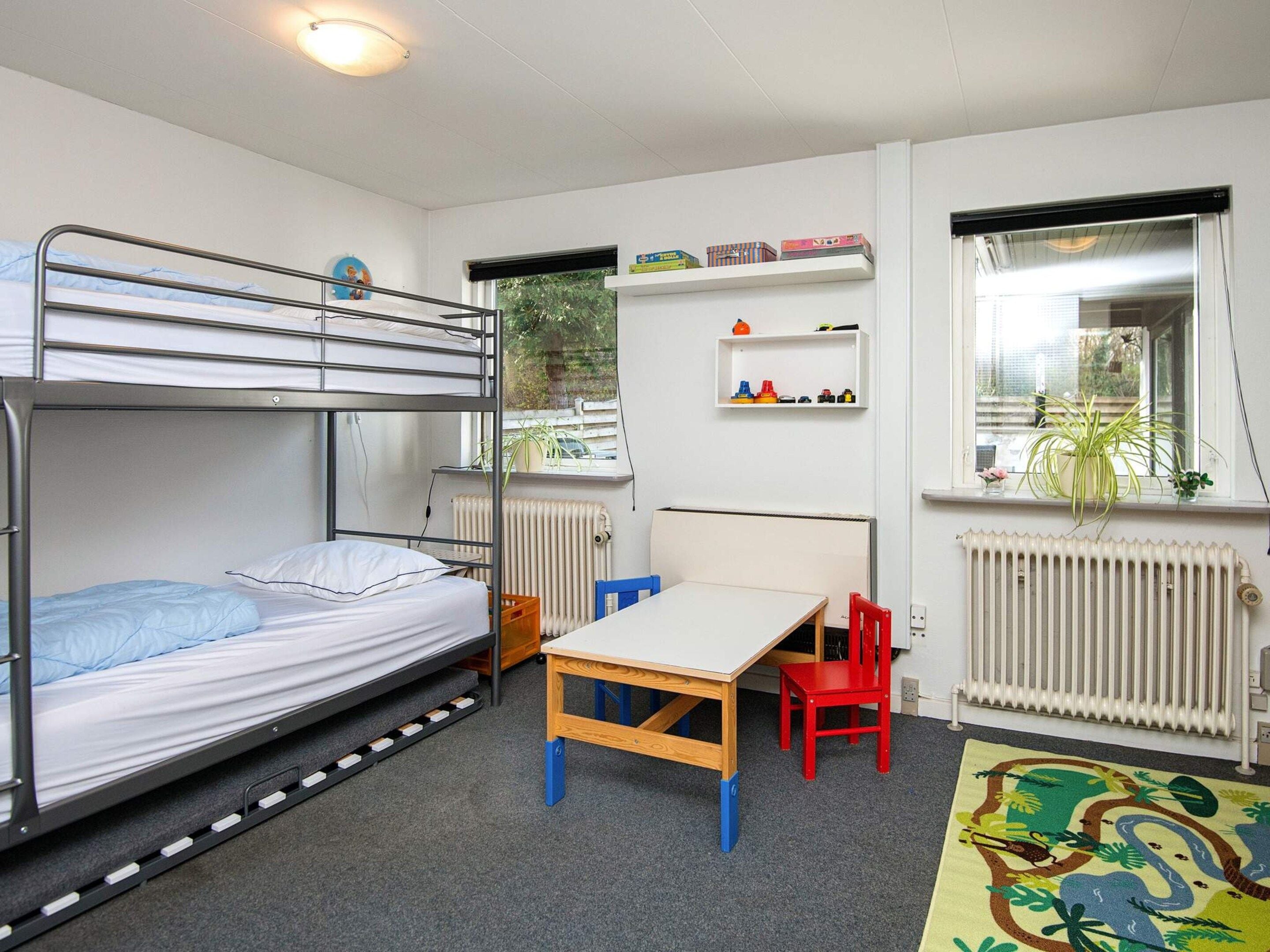 A bunk bed with a desk and chair, a radiator, a window with a plant, and a shelf with toys.