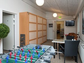 A room with a foosball table, a television mounted on the wall, and a seating area with a chair and table.