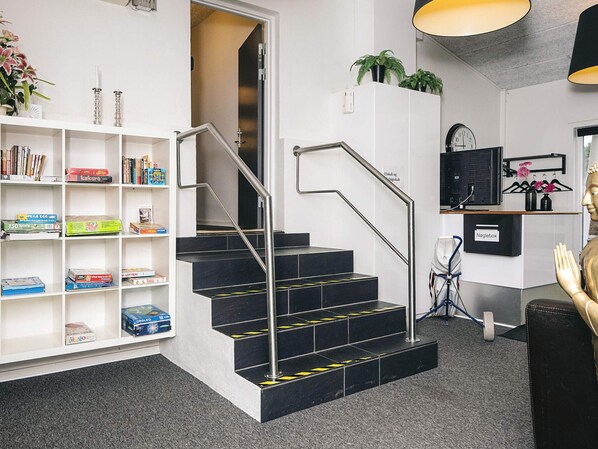 A staircase with metal railings leading to a landing, a white bookshelf filled with books and games, a clock on the wall, and a statue on the right.