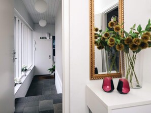 A hallway with a white door, a staircase, and a mirror with a gold frame reflecting a vase of flowers.