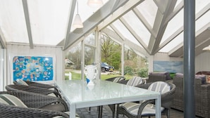 A covered patio area with wicker furniture, a glass table, and a view of the outdoors. - 4 Star Holiday Home in Oksbol (Oksbol)