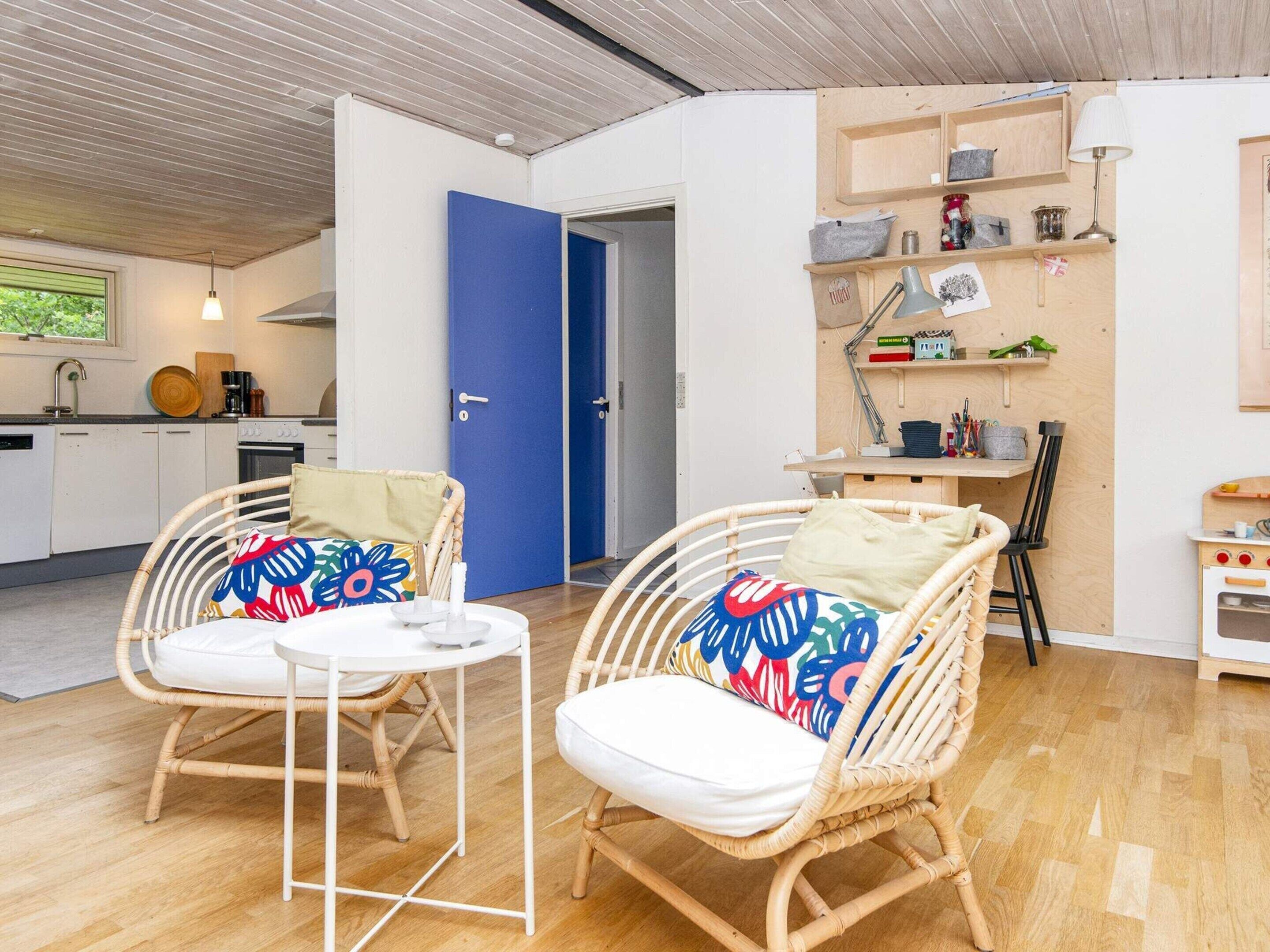 Una habitación acogedora con sillas de mimbre, una mesita redonda y una zona de cocina con una puerta azul.