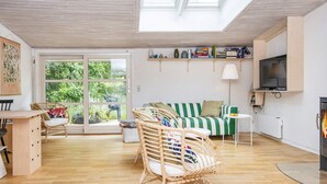 A spacious living room with a high ceiling, a green-striped sofa, a wicker chair, a dining area with a wooden table, and a television mounted on the wall. - 6 Person Holiday Home in Knebel-by Traum (Knebel)