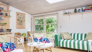 A cozy living room with a green and white striped sofa, wicker chairs, a small round table, and a window with a view of greenery. - 6 Person Holiday Home in Knebel-by Traum (Knebel)