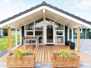 Un espace extérieur abrité, doté d’une terrasse en bois, d’une table avec des chaises et de jardinières remplies de plantes vertes.