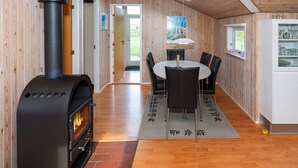Een modern interieur met een houten lambrisering, een zwarte open haard, een ronde eettafel met stoelen en een raam met uitzicht.