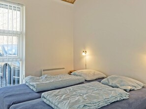 A bedroom with a bed, a radiator, a window, and a wall-mounted lamp.