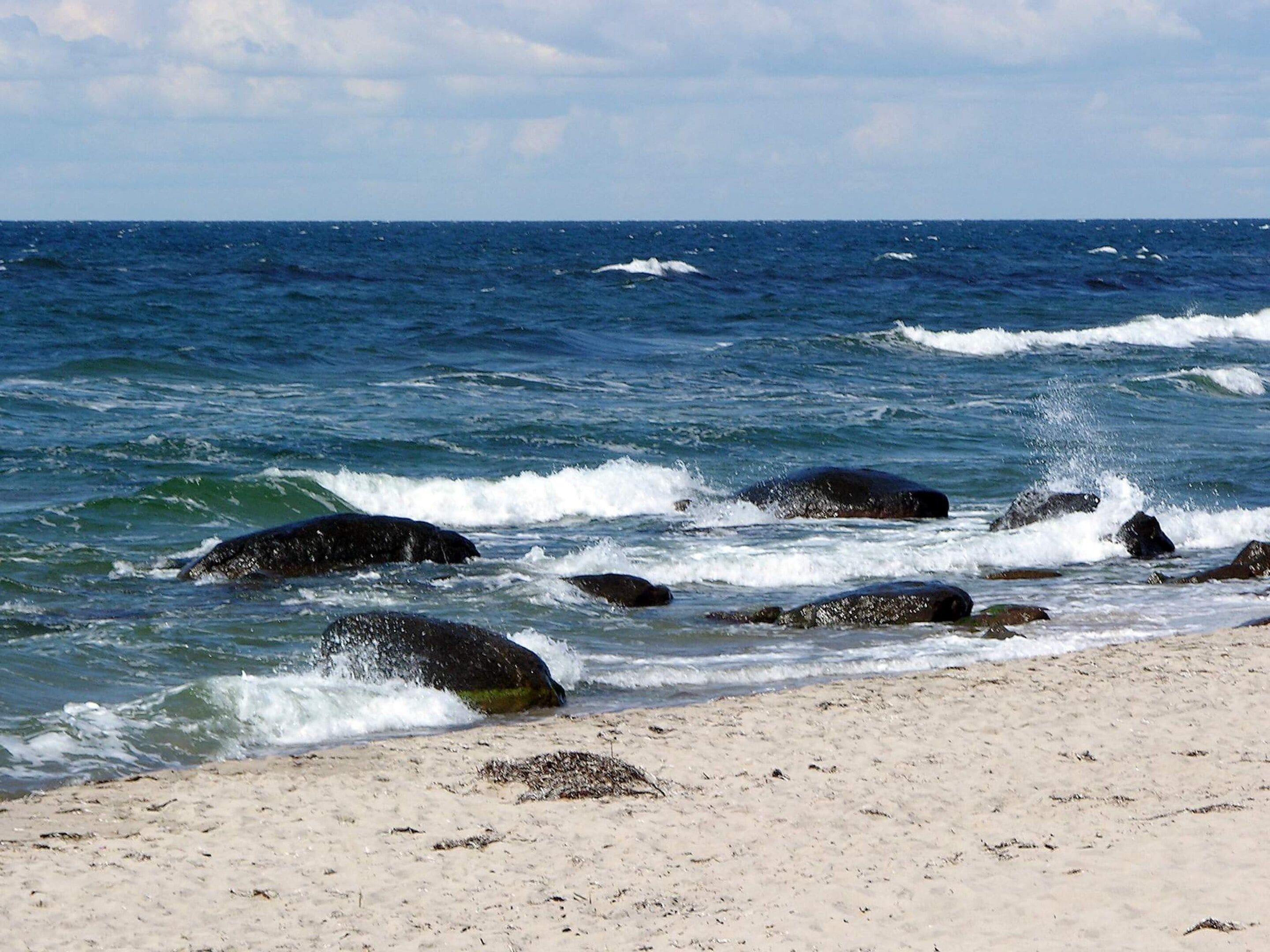 Ein Strand mit brechenden Wellen an Felsen und blauem Himmel.