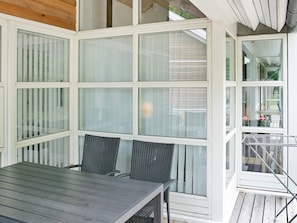 A covered patio with a table and chairs, large windows, and a view of the street.