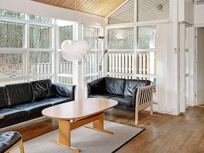 A modern interior with a wooden table, black leather sofas, and a large window with a view of trees.