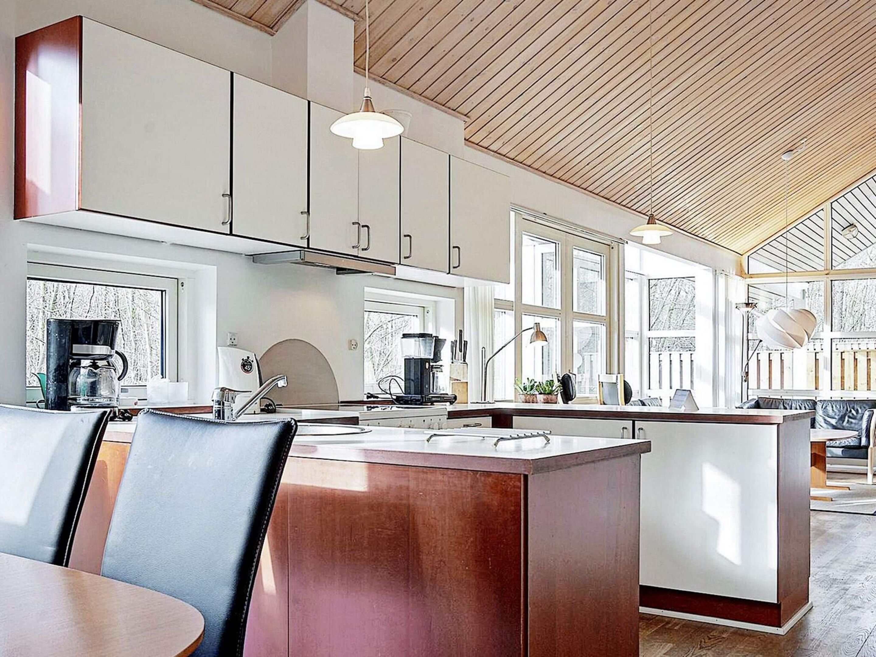 A modern kitchen with a central island, pendant lighting, and large windows.