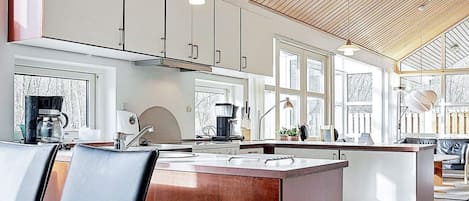A modern kitchen with a central island, pendant lighting, and large windows.