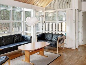 A modern living room with a wooden table, black leather sofas, and large windows.