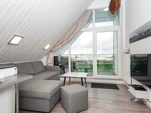 A modern loft-style room with a high ceiling, a sofa, a dining table, and a TV. - Holiday Home in Wendtorf (Wendtorf)