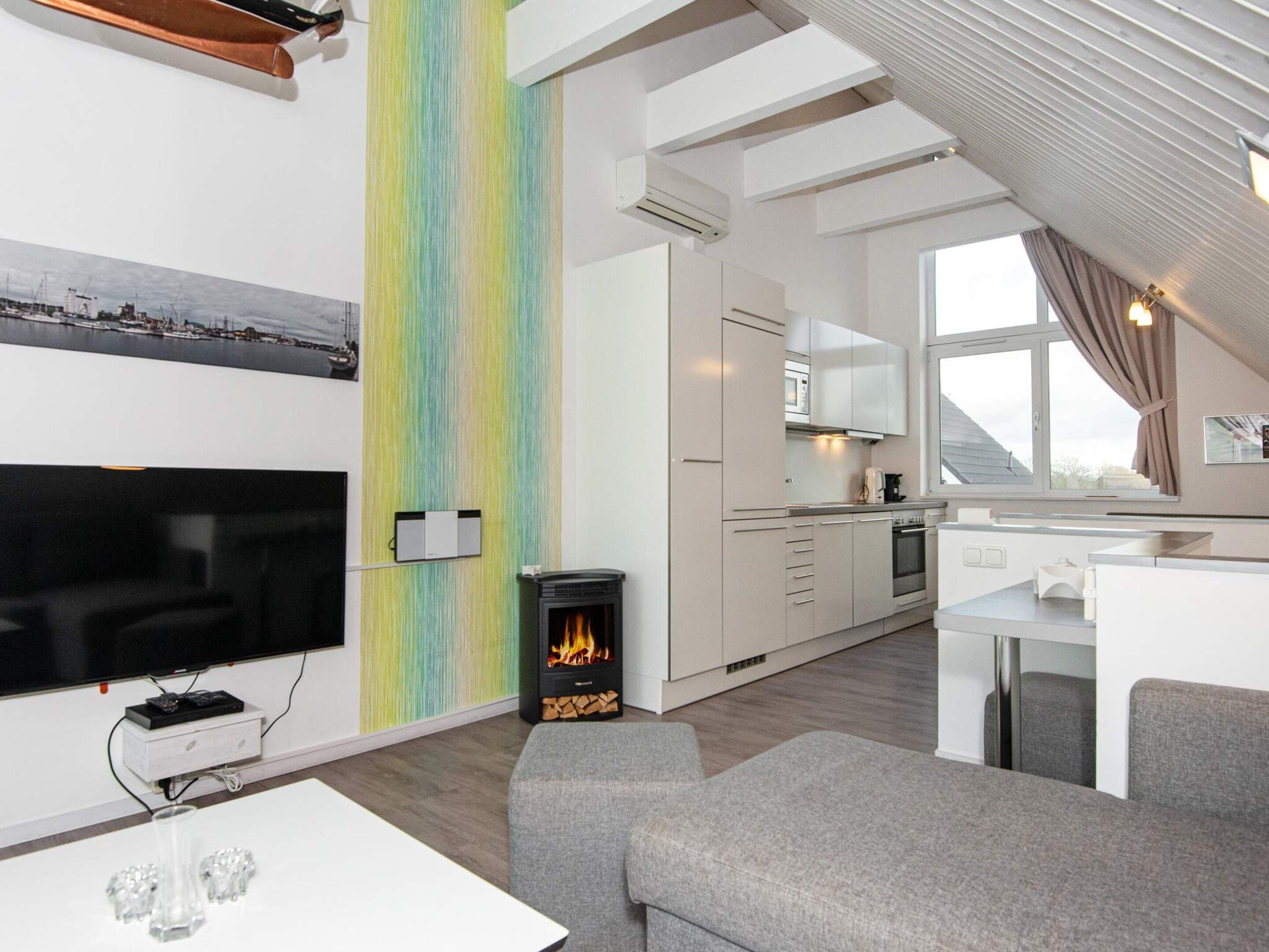 A modern living room with a flat-screen TV, a fireplace, and a dining area with a kitchen in the background.