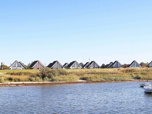 A row of modern houses with large windows, a grassy area in front, and a body of water with boats. - Holiday Home in Wendtorf (Wendtorf)