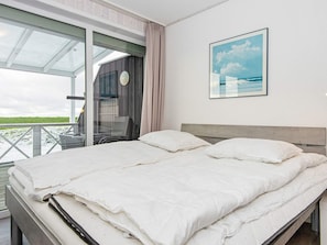 A bedroom with a bed, a window with curtains, a clock, and a framed picture on the wall. - Holiday Home in Wendtorf (Wendtorf)
