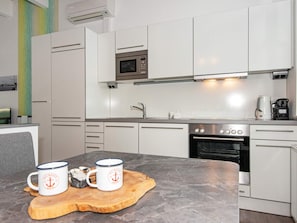 A modern kitchen with white cabinets, a microwave, a sink, and a stove. There are two mugs on a wooden tray. - Holiday Home in Wendtorf (Wendtorf)