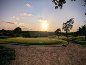 A golf course with a dirt path, trees, and a clear sky.