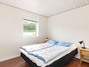 A bedroom with a bed, a nightstand, a lamp, and a window with a view of greenery.