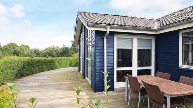 A house with a covered patio, a dining table with chairs, and a view of the surrounding greenery. - 5 Star Holiday Home in Skals (Skals)