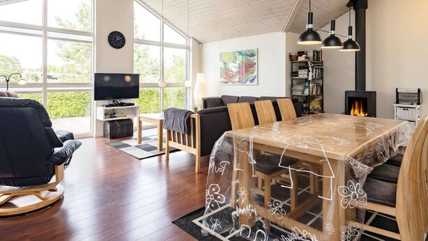 A spacious living area with a wooden dining table, a sofa, a TV, and a fireplace. - 5 Star Holiday Home in Skals (Skals)