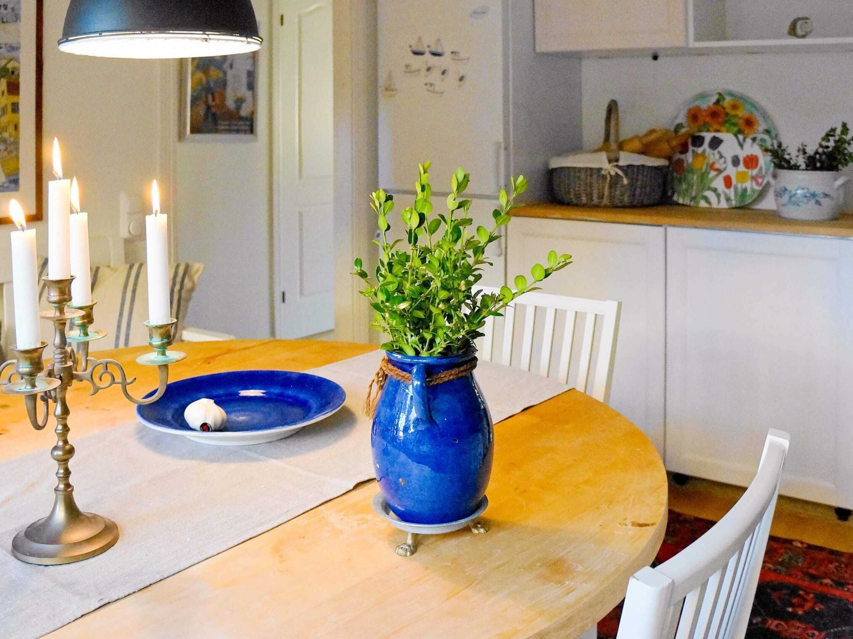 A dining table with a blue vase, white candles, and a blue plate.