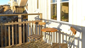 A wooden deck with a table and chairs, a white building with a balcony, and a rocky landscape in the background. - Holiday Home in Skärhamn (Skaerhamn)