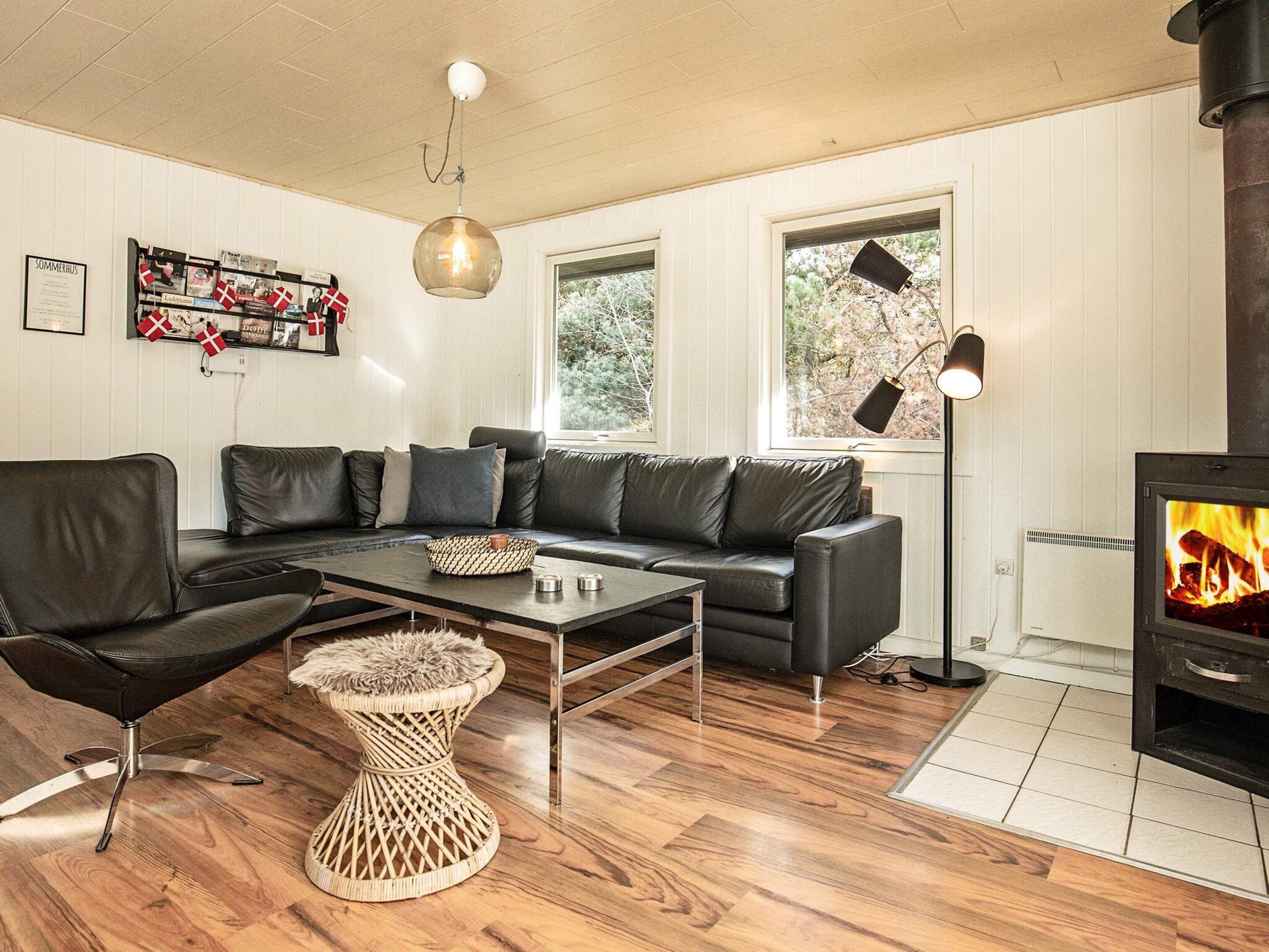 A modern living room with a leather sofa, a coffee table, a wicker side table, and a wood-burning stove.