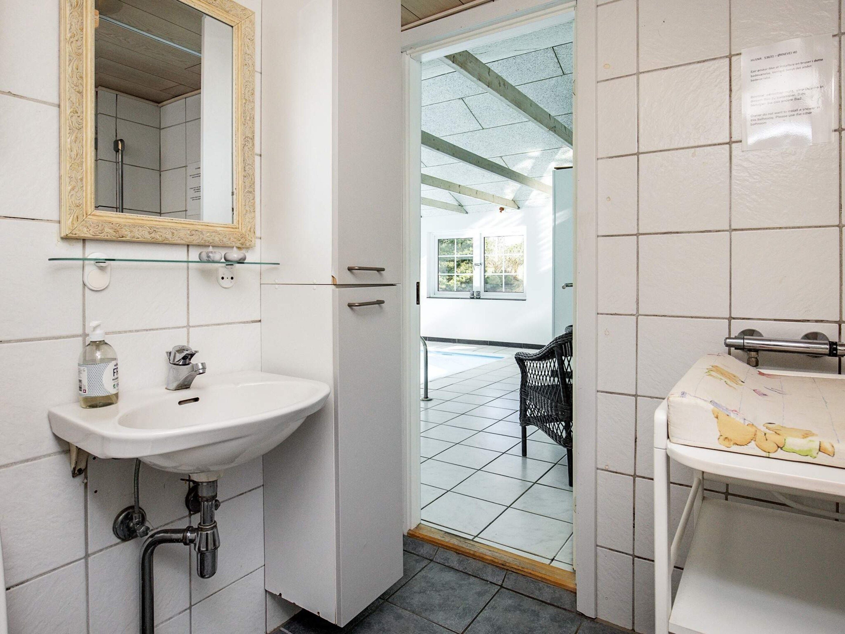 Ein Badezimmer mit einem weißen Waschbecken, einem Spiegel und einer Glasablage.